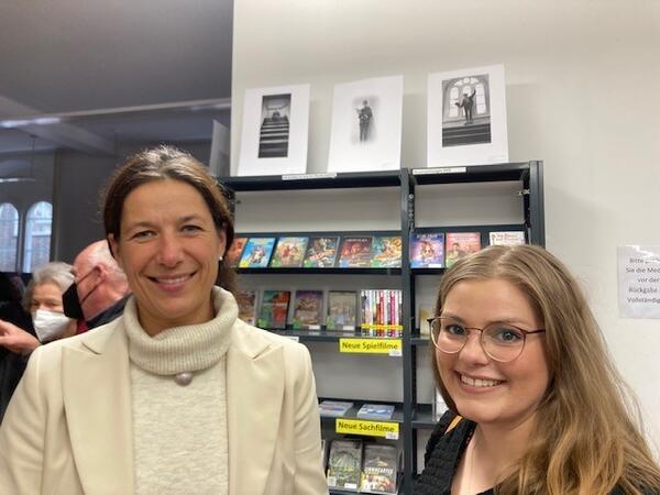 Bild vergrößern: Samtgemeindebürgermeisterin Claudia und Büchereileiterin Lisa Röper auf der Jugendbuchwoche vor einem Bücherregal.