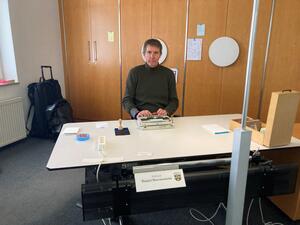 Bild vergrößern: Der Künstler Daniel Hoernemann sitzt an einem Schreibtisch mit einer weißen Arbeitsplatte.