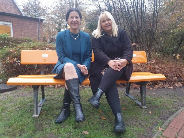 Samtgemeindebürgermeisterin Claudia Sommer und die Gleichstellungsbeauftragte Evelyn Hollmann sitzen auf einer orangen Bank.