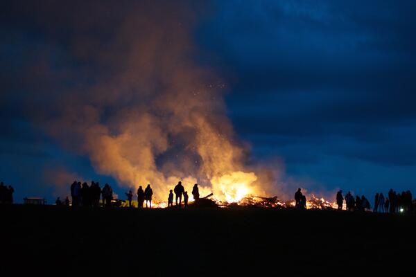 Ein großes Osterfeuer brennt mit Personen im Vordergrund.