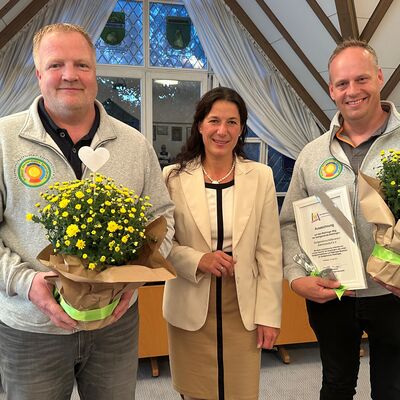 Bild vergr&ouml;&szlig;ern: Marco Hinrichs, mit einer gelben Blume in den H&auml;nden, Claudia Sommer und Nico Rickens mit der Ehrenurkunde l&auml;cheln in die Kamera.