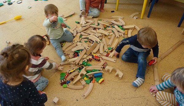 Bild vergr&ouml;&szlig;ern: Kinder sitzen im Kreis um Teile einer Holz-Eisenbahn.
