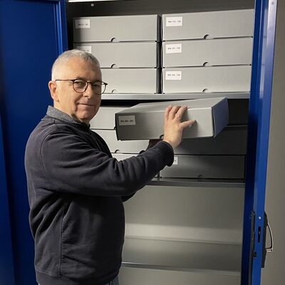 Bild vergr&ouml;&szlig;ern: Herr Thunich steht vor einem Schrank, in dem viele graue K�sten stehen und h�lt eine Kiste in den H�nden.
