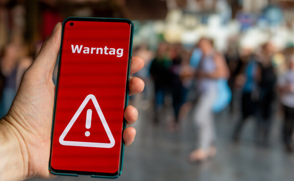 Bild vergr&ouml;&szlig;ern: Eine Hand h�lt ein Handy. Der Bildschirm ist knallrot und zeigt in wei�en Buchstaben WARNTAG und ein Dreieck mit Ausrufezeichen.